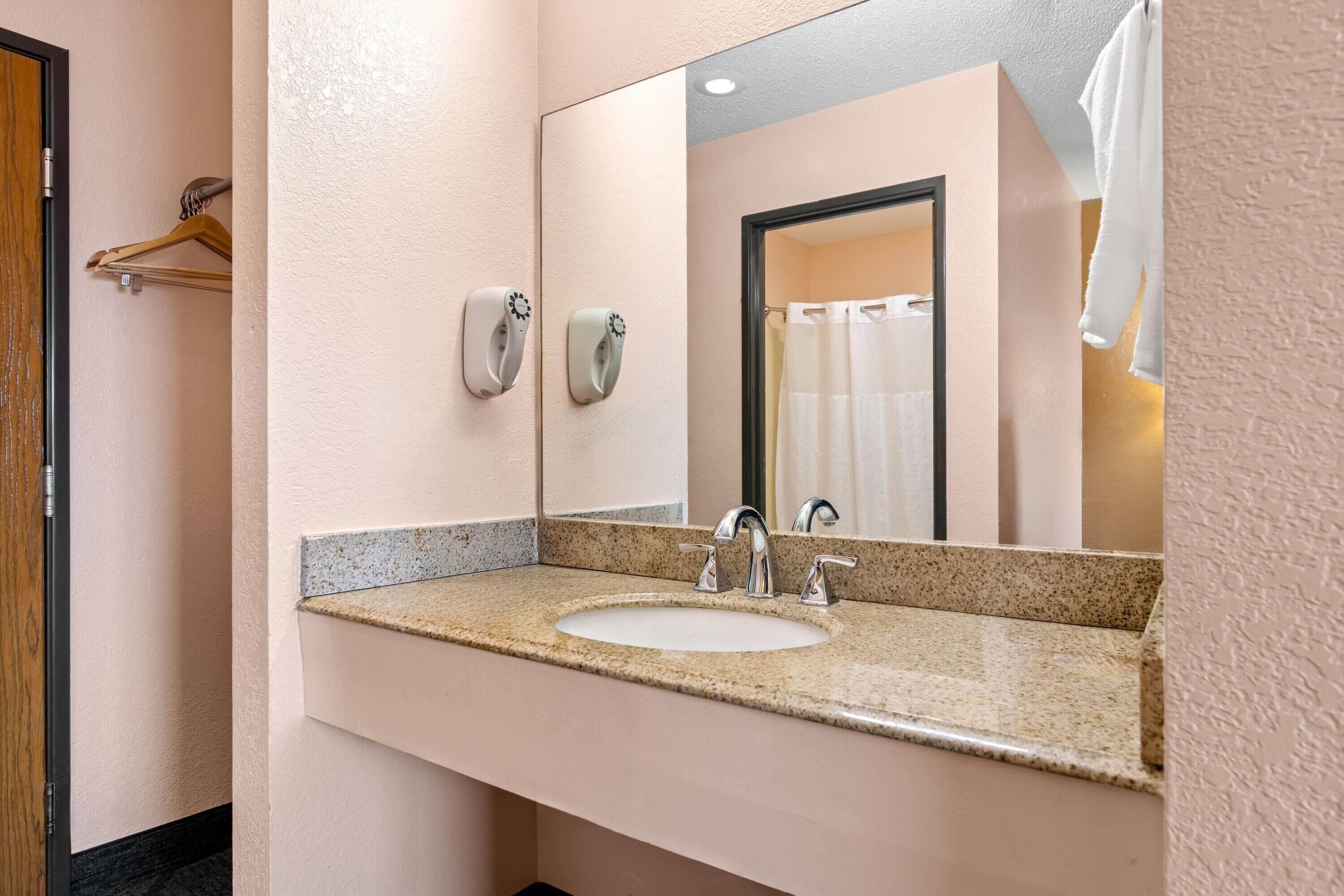 A bathroom with a sink, mirror, towel dispenser, and shower curtain.