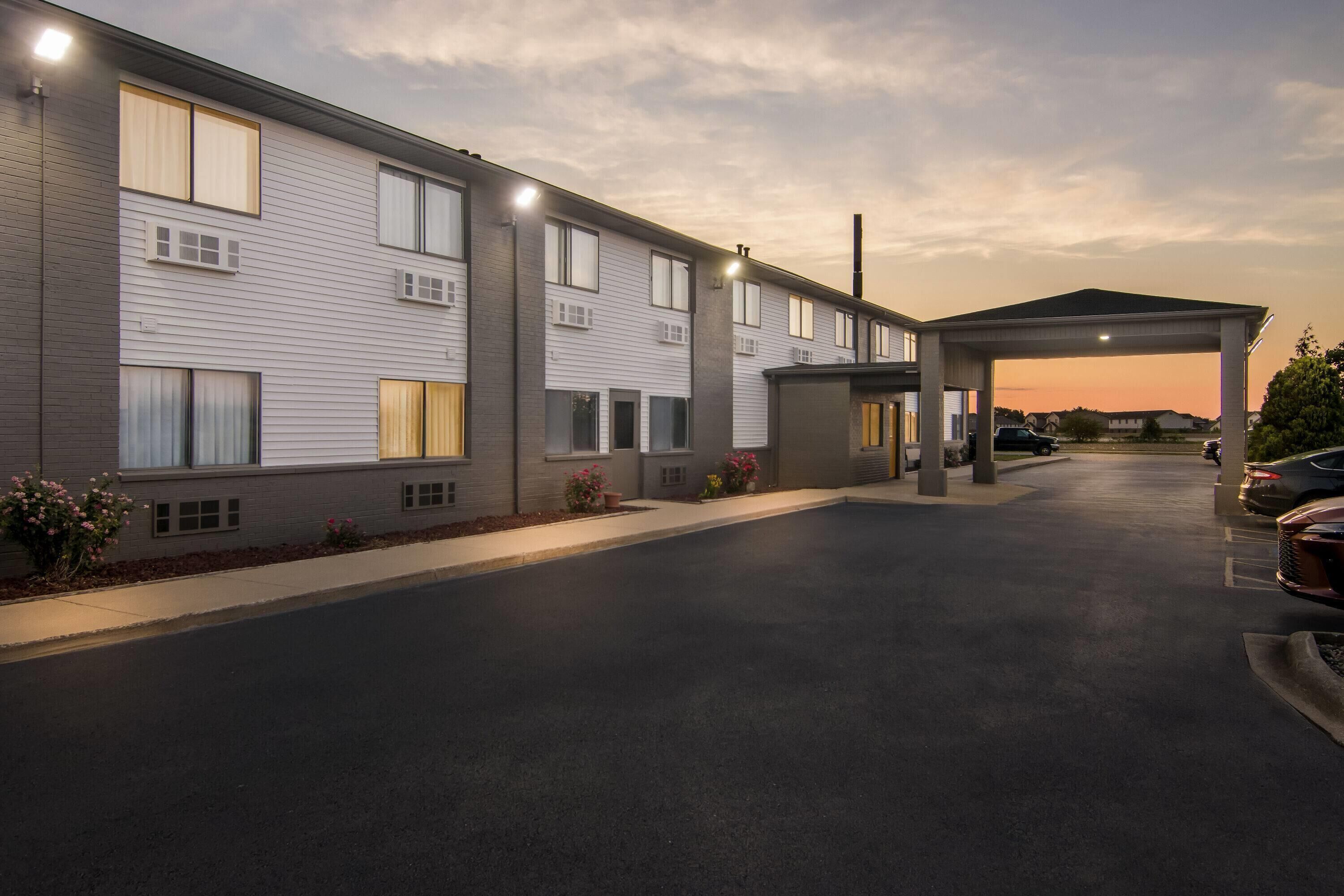 Un hôtel à plusieurs étages, doté d’un parking couvert et d’une rangée de voitures garées.