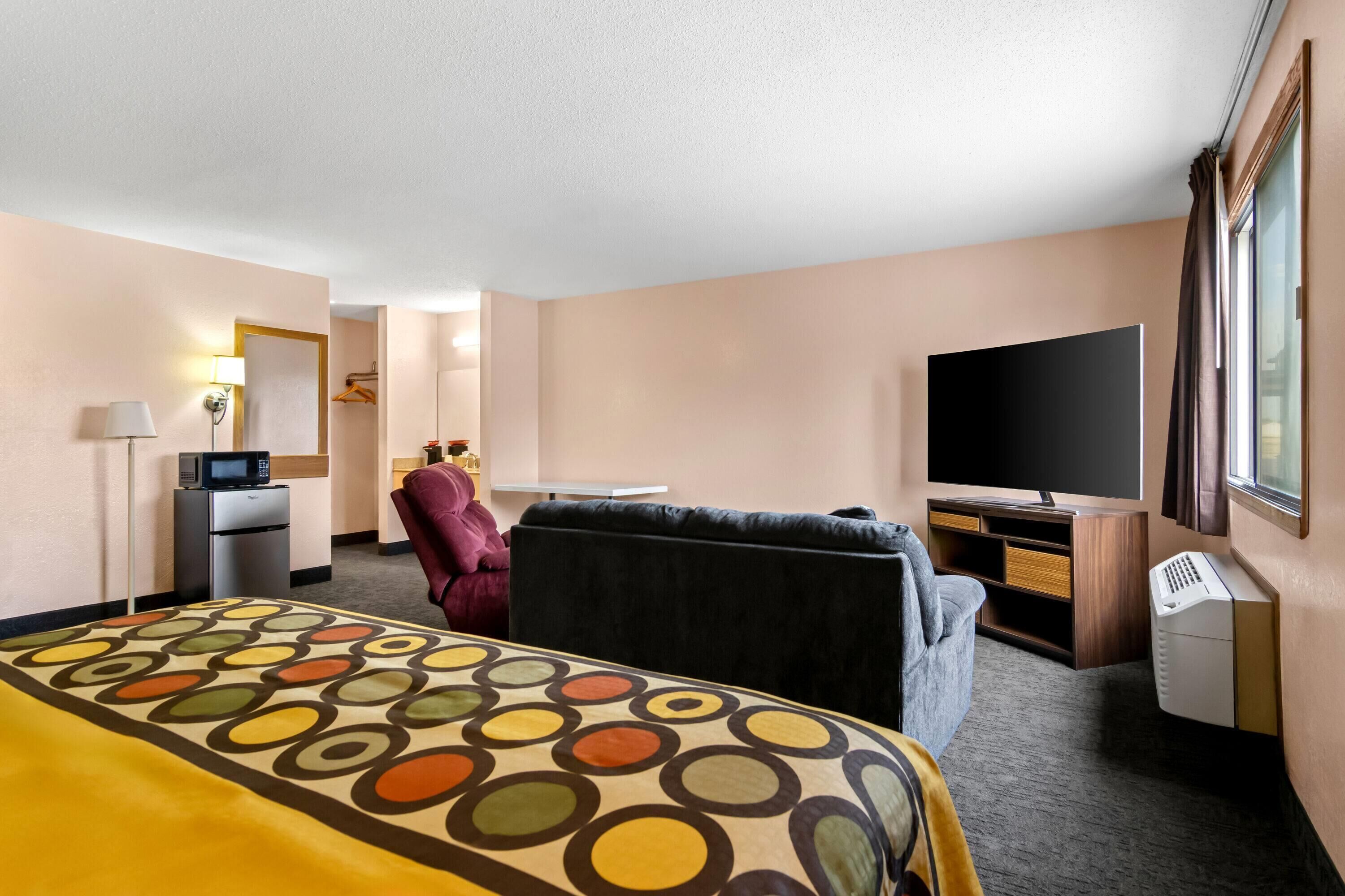 A hotel room with a bed, a desk, a chair, a television, and a window.