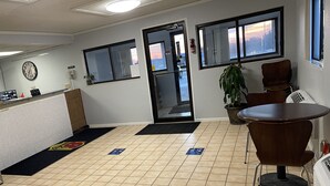 A reception area with a clock, a reception desk, a plant, a chair, and a view of the outside through a window. - Super 8 by Wyndham Dixon (Dixon)