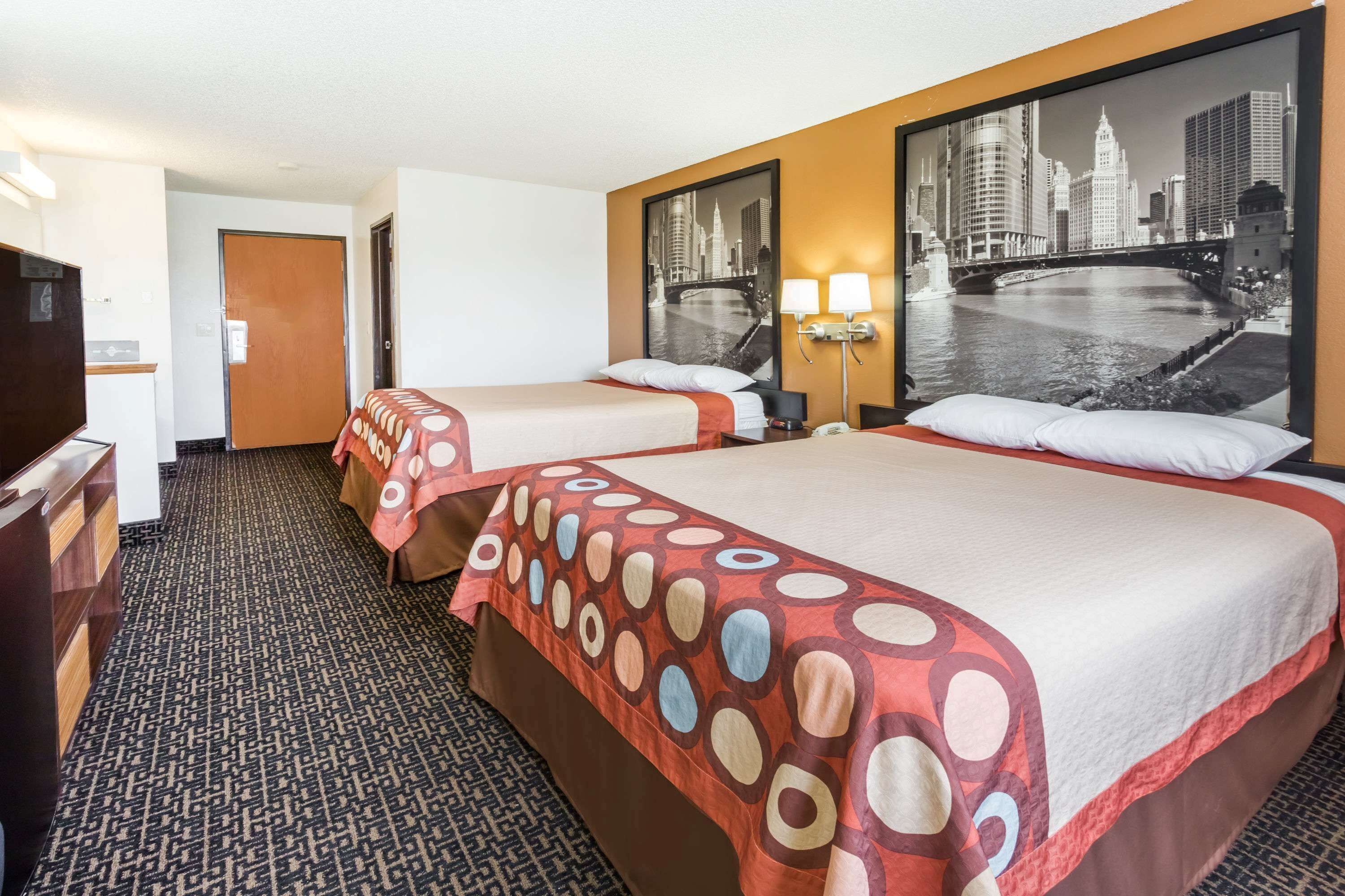 A hotel room with two beds, a cityscape view, a desk, and a patterned carpet.