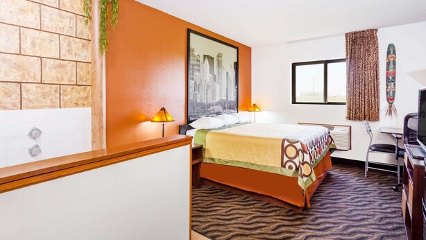 A hotel room with a brick-patterned wall, a bed with a patterned bedspread, a cityscape picture, a window with curtains, and a desk with a chair. - Super 8 by Wyndham Dixon (Dixon)