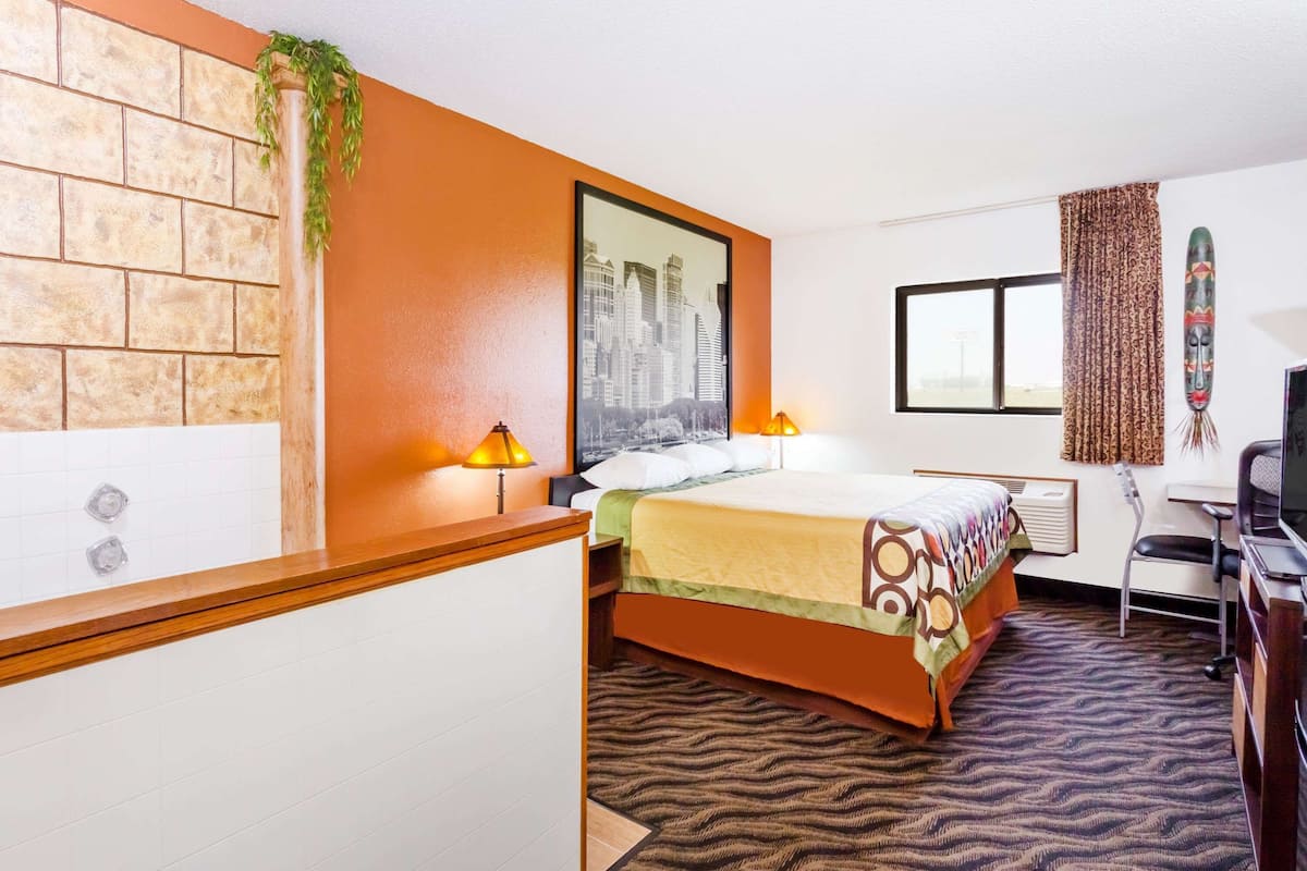 Une chambre d’hôtel avec un mur décoré d’un motif en briques, un lit recouvert d’une couvre-lit à motifs, un tableau représentant un paysage urbain, une fenêtre avec des rideaux et un bureau avec une chaise.