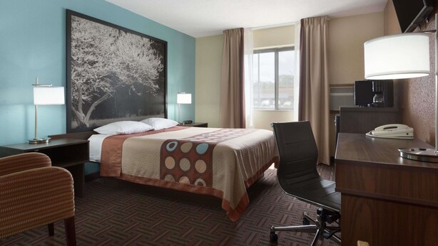 Habitación de hotel con cama, escritorio, silla, televisor y ventana con cortinas.