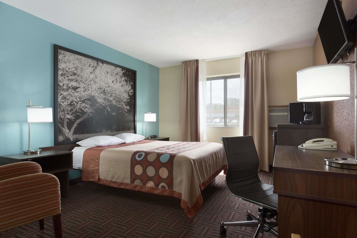 A hotel room with a bed, a desk, a chair, a TV, and a window with curtains.