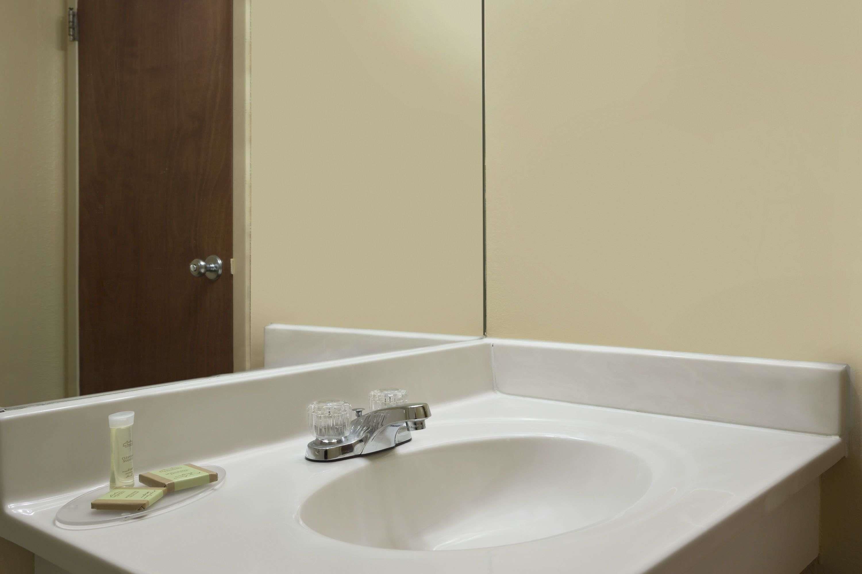 A white bathroom sink with a mirror above it, a wooden door to the left, and a white countertop.