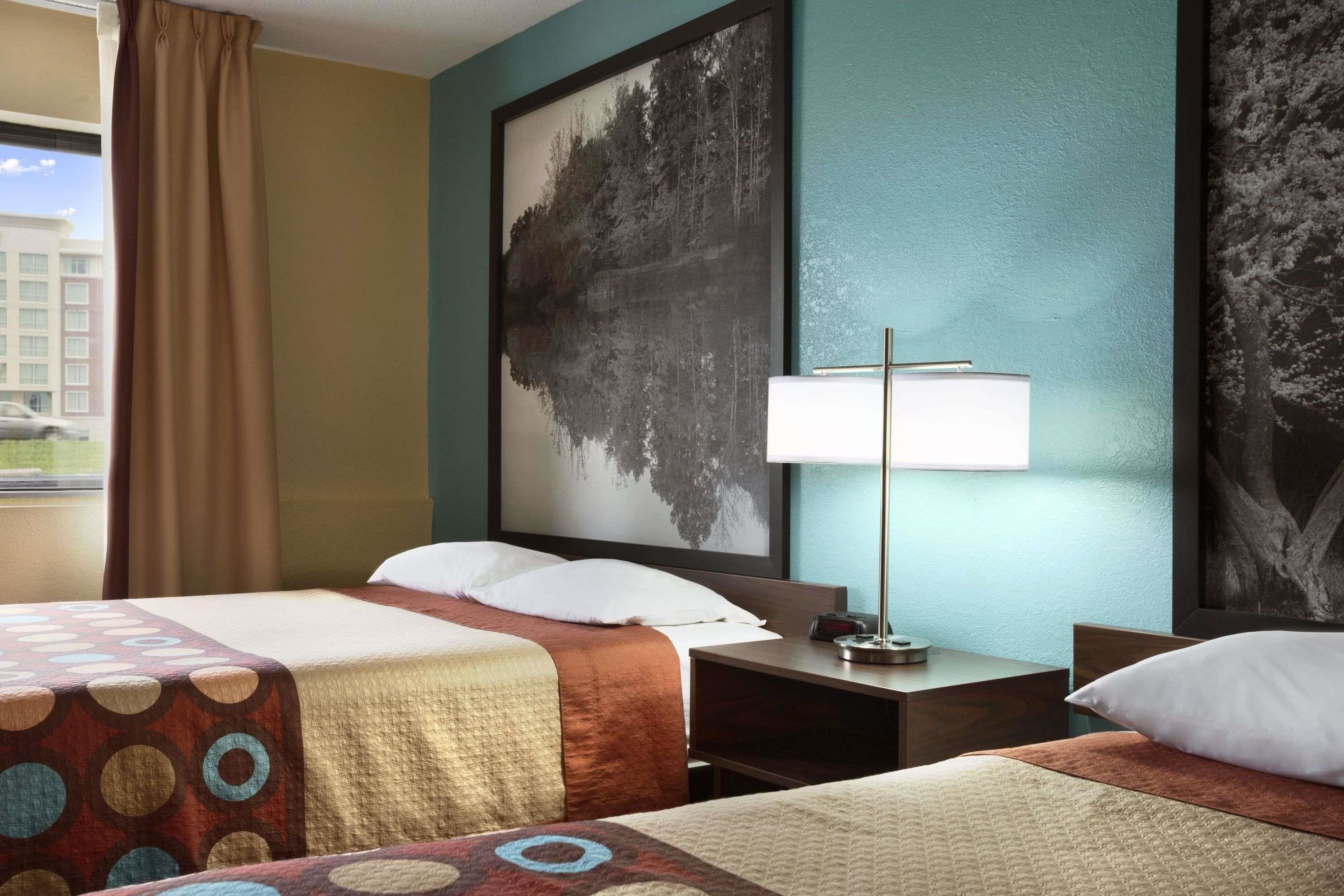 A hotel room with two beds, a nightstand, a lamp, and a large framed picture on the wall.