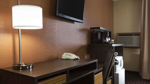 Habitación de hotel con escritorio, lámpara, televisor de pantalla plana, teléfono, microondas y contenedor de basura.