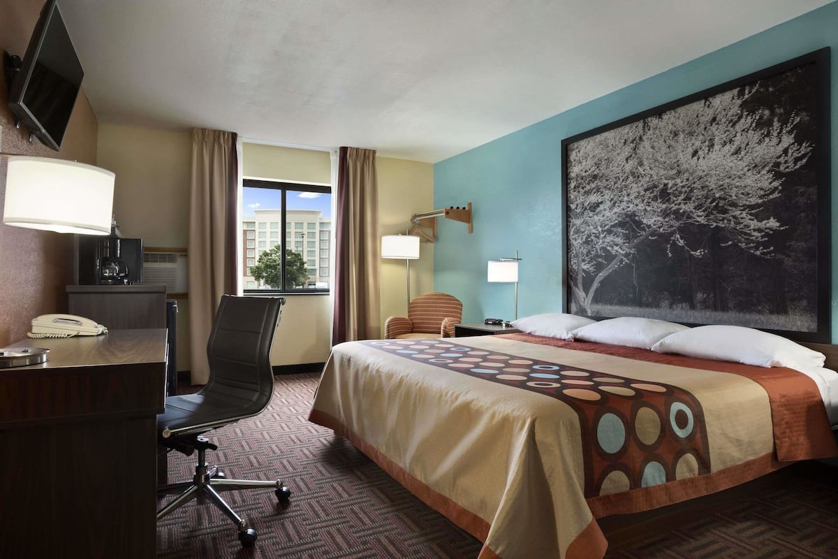 A hotel room with a bed, desk, chair, and a large window.