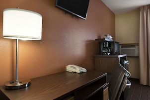 Habitación de hotel con escritorio, lámpara, teléfono, televisor montado en la pared, cafetera y equipo de aire acondicionado.