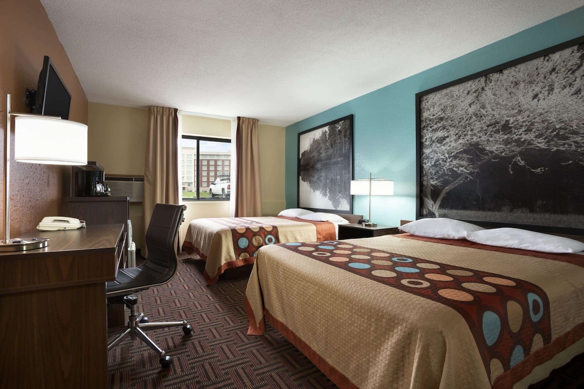 A hotel room with two beds, a desk, a chair, a TV, and a large window.