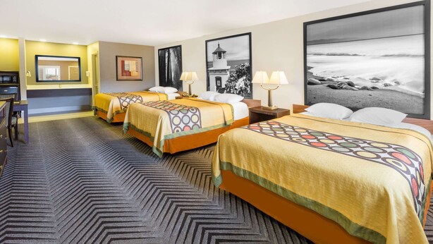 A hotel room with three beds, a desk, and a large framed photograph of a beach. - Super 8 by Wyndham Fortuna (Fortuna)