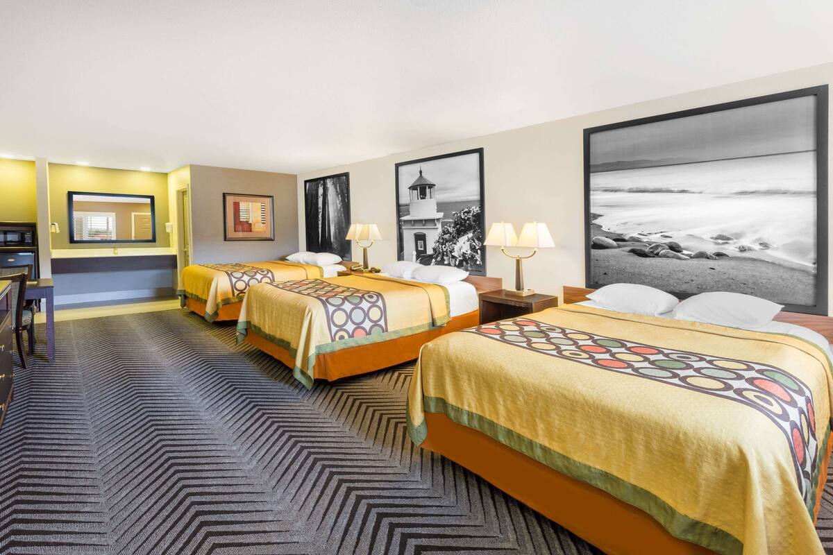A hotel room with three beds, a desk, and a large framed photograph of a beach.