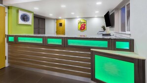 A reception area with a wooden counter, a 'Super 8' sign, a framed picture, and a TV on the wall. - Super 8 by Wyndham Fortuna (Fortuna)