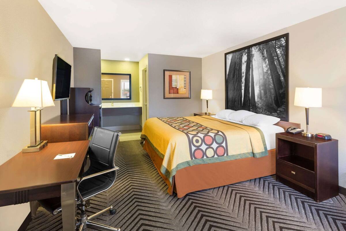 A hotel room with a bed, desk, chair, and a large painting on the wall.