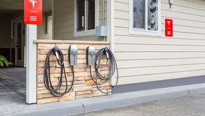 A Tesla electric vehicle charging station with two charging cables, a stone wall, and a house entrance with windows. - Super 8 by Wyndham Fortuna (Fortuna)