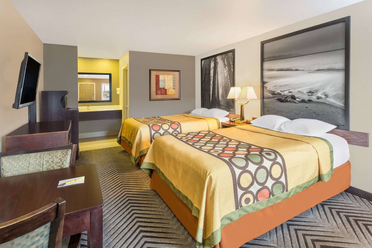 A hotel room with two beds, a desk, a TV, and a large beach-themed painting.