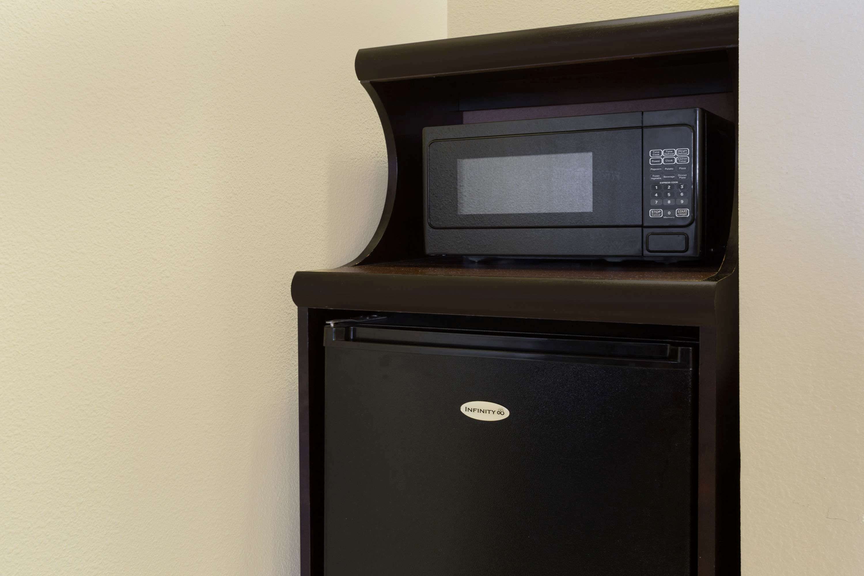 A black microwave on a wooden counter with a small refrigerator below it.