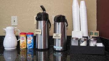 A coffee station with a coffee maker, hot water dispenser, and condiment dispensers.