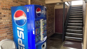 Un distributeur de Pepsi situé dans un bâtiment dont le mur est en briques et qui possède un escalier.