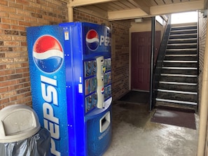 Un distributeur de Pepsi situé dans un bâtiment dont le mur est en briques et qui possède un escalier.