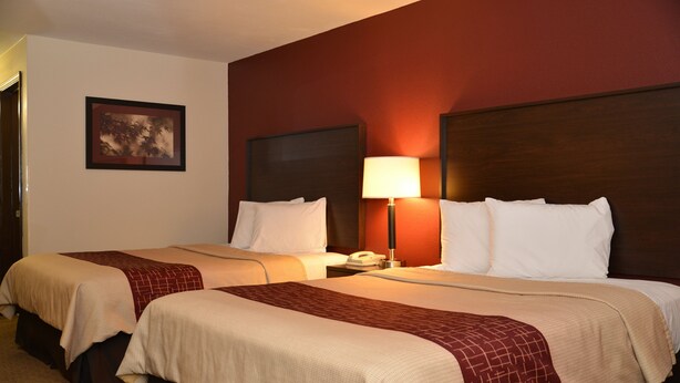 Une chambre d’hôtel avec deux lits, une table de chevet avec une lampe, un téléphone et un tableau encadré au mur.