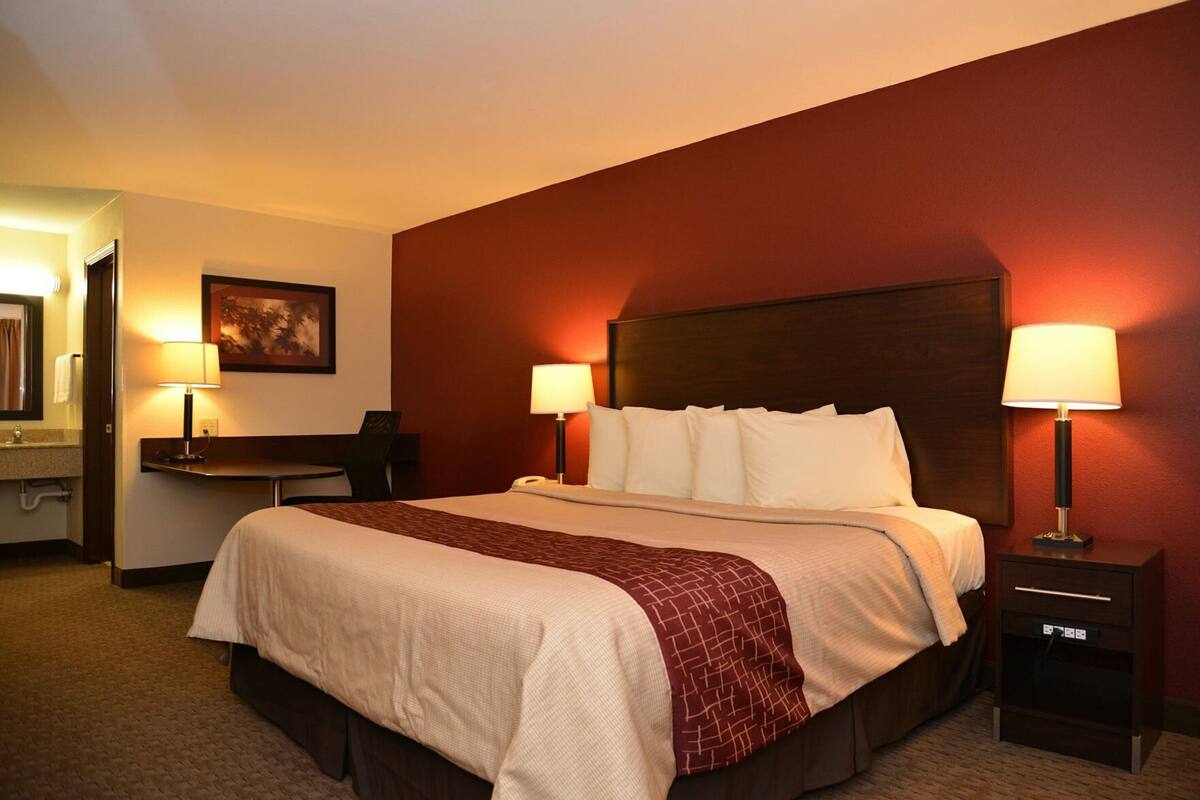 A hotel room with a large bed, two bedside lamps, a desk with a chair, a mirror, and a painting on the wall.