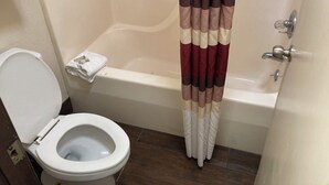 Une salle de bain avec des toilettes blanches, une baignoire et un rideau de douche à rayures marron et beige, ainsi qu’une serviette blanche sur le sol.