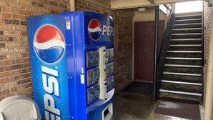A Pepsi vending machine in a hallway with a brick wall and a staircase. - Red Roof Inn Cookeville - Tennessee Tech (Cookeville)