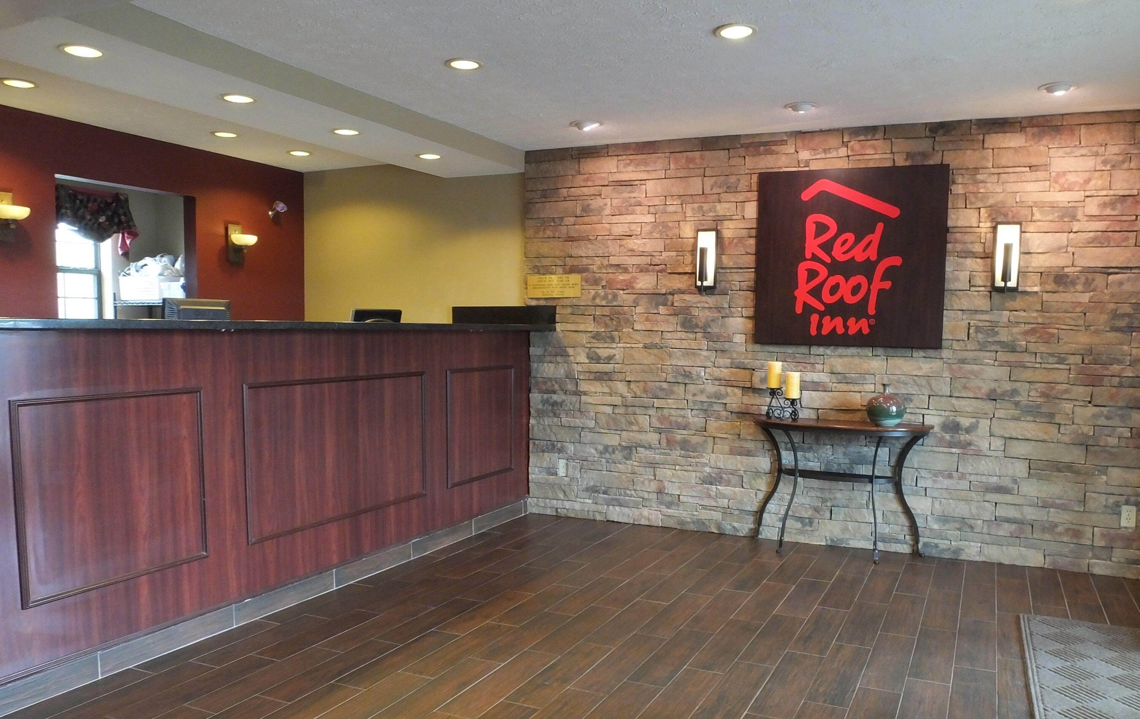 Un espace d’accueil avec un comptoir de réception en bois, un mur en pierre et une enseigne Red Roof Inn.