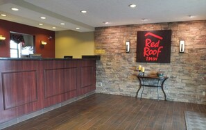 A reception area with a wooden reception desk, a stone wall, and a Red Roof Inn sign. - Red Roof Inn Cookeville - Tennessee Tech (Cookeville)