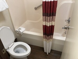 A bathroom with a white toilet, a bathtub with a brown and beige striped shower curtain, and a white towel on the floor. - Red Roof Inn Cookeville - Tennessee Tech (Cookeville)