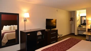 Habitación de hotel con cama, televisión, escritorio, espejo y baño visible a través de una puerta abierta.