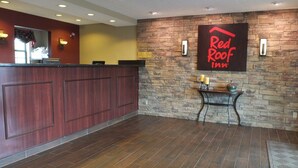 A reception area with a wooden reception desk, a stone wall, and a Red Roof Inn sign. - Red Roof Inn Cookeville - Tennessee Tech (Cookeville)