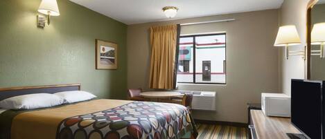 Habitación de hotel con cama, escritorio con computadora, televisión, ventana con cortinas y un cuadro en la pared.