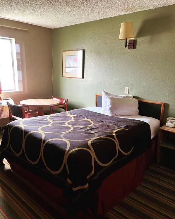 Une chambre d’hôtel avec un lit, une table de chevet, une lampe, une chaise et une petite table.