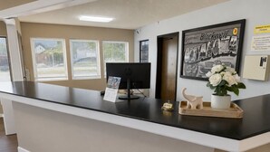 Una mesa de recepción con una computadora, un cartel de bienvenida enmarcado y una planta pequeña.