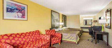 A hotel room with a sofa, two single beds, a desk, and a chair.