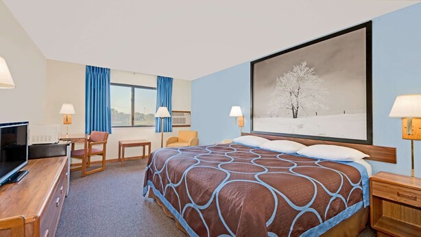 A hotel room with a large bed, a desk with a TV, a chair, and a window with curtains. - Super 8 by Wyndham Centerville (Centerville)