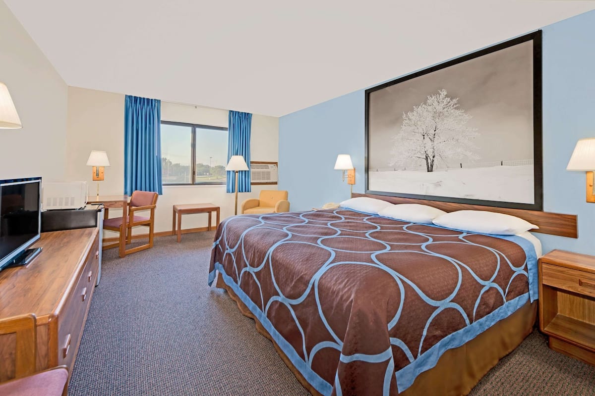 A hotel room with a large bed, a desk with a TV, a chair, and a window with curtains.