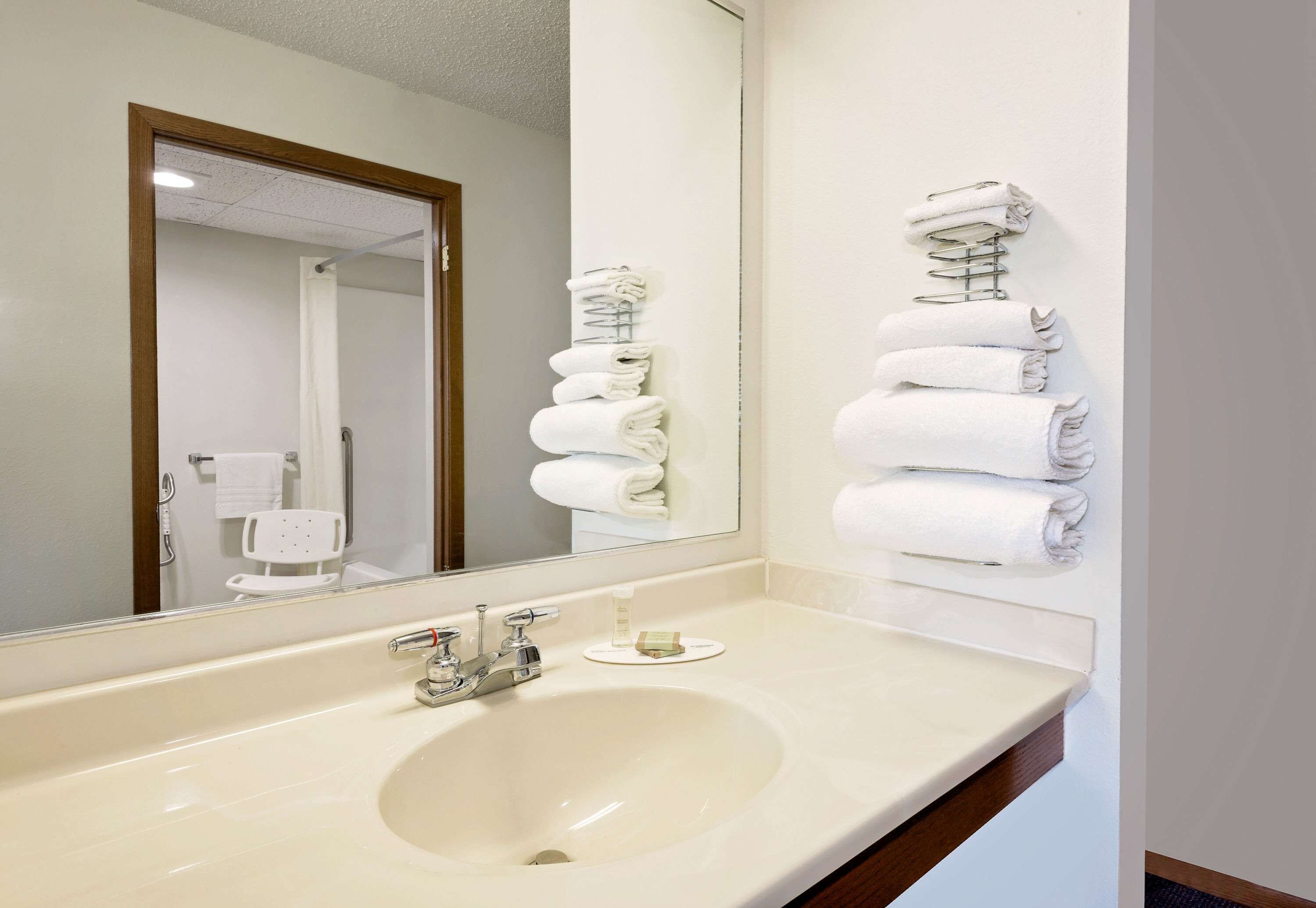 Un baño de hotel con un lavamanos grande, un espejo y toallas apiladas en un perchero.