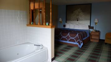 A hotel room with a large white bathtub, a bed with a blue and brown patterned bedspread, and a nightstand with two lamps.