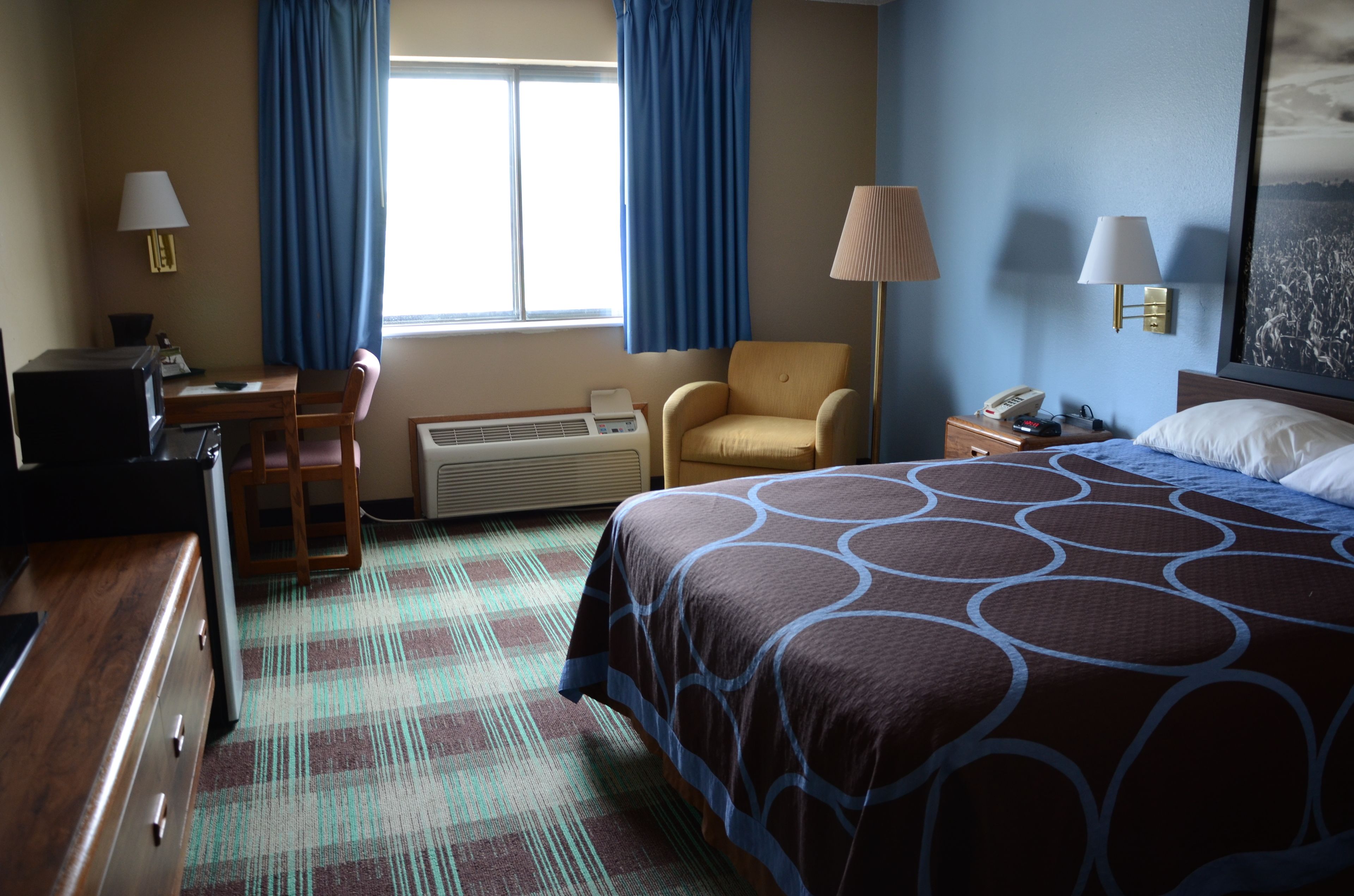 A hotel room with a bed, desk, chair, and a heater.