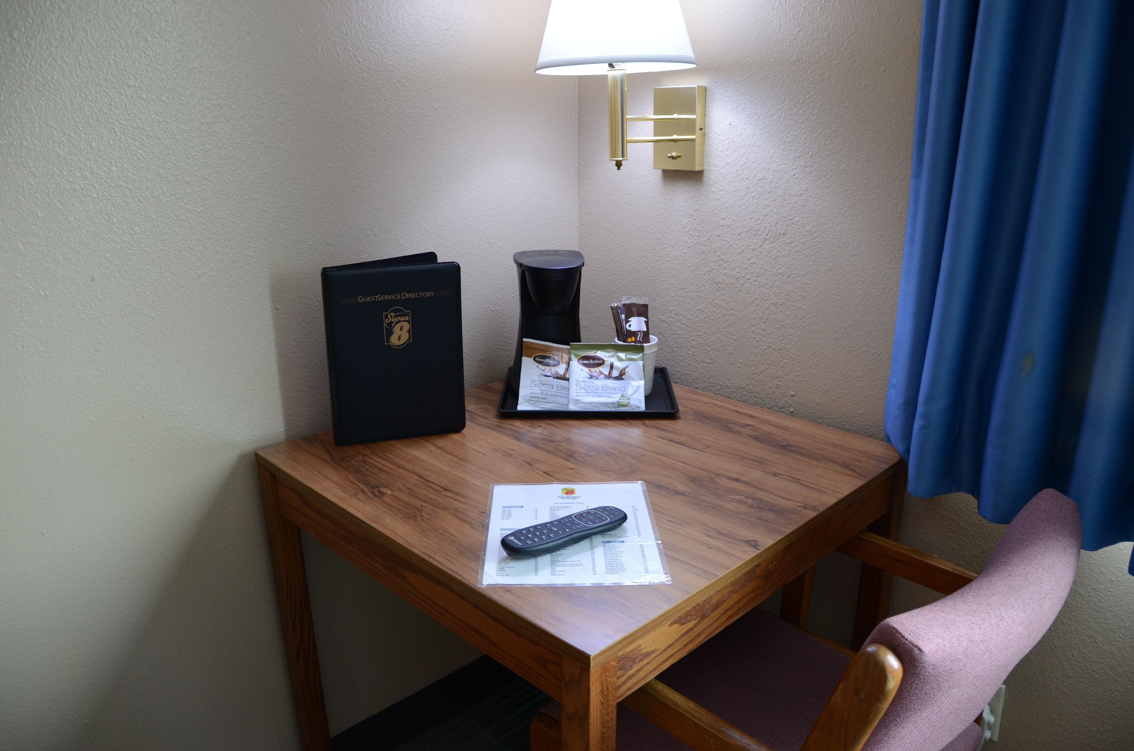 A wooden desk with a remote control, a black folder, and a tray with a coffee cup and a tissue box.