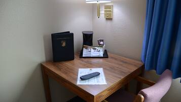 A wooden desk with a remote control, a black folder, and a tray with a coffee cup and a tissue box.