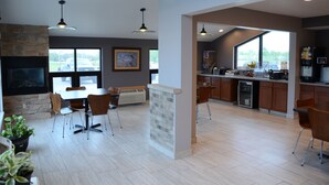 A modern kitchen with a stone fireplace, dining area with chairs, and a large window offering a view of the outdoors. - Super 8 by Wyndham Centerville (Centerville)