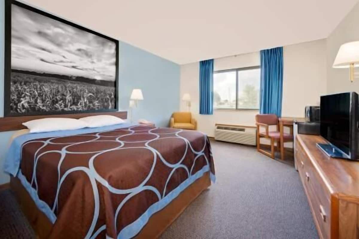 Una habitación de hotel con cama, escritorio, televisor y un amplio ventanal con cortinas.