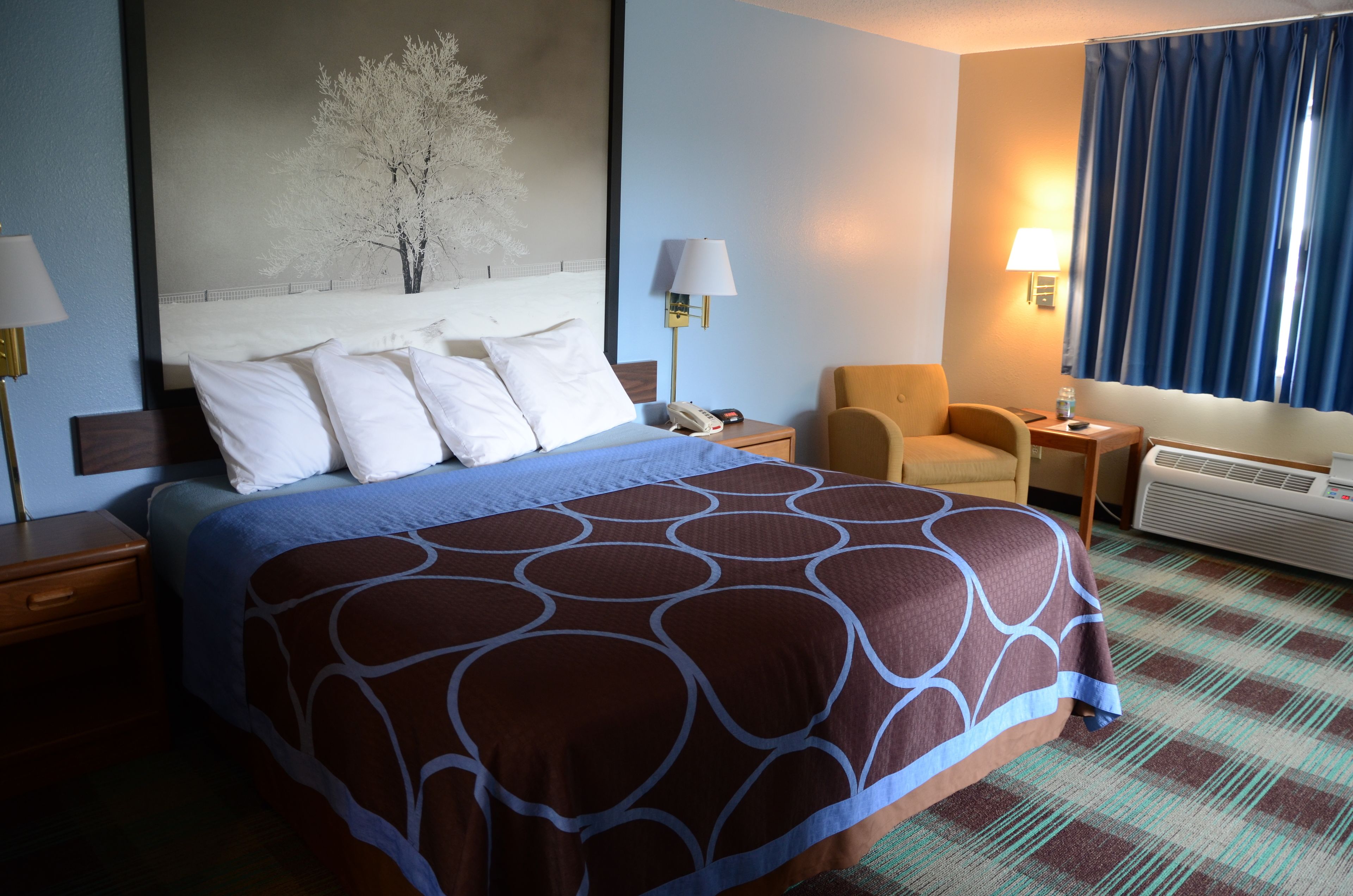 Habitación de hotel con una cama grande, una silla, un escritorio y un aire acondicionado instalado en la pared.