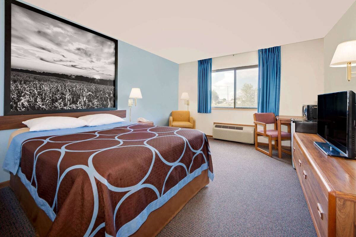 A hotel room with a large bed, a desk, a chair, a television, and a large window with curtains.