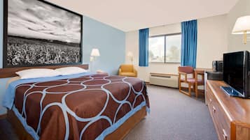Habitación de hotel con una cama grande, un escritorio, una silla, un televisor y un ventanal con cortinas.